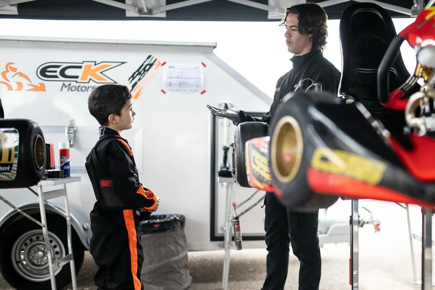 Un entrenador de ECK explica a un piloto joven junto al remolque del equipo